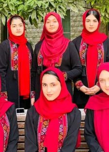 A group of ten women wearing black outfits with red embroidered patterns and bright red headscarves