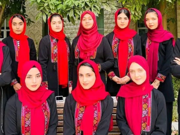 A group of ten women wearing black outfits with red embroidered patterns and bright red headscarves