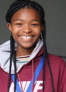 Smiling girl with braided hair wearing a maroon hoodie and blue lanyard