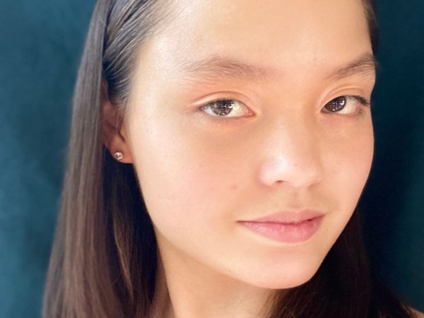A young woman with long dark hair and subtle makeup looks calmly at the camera