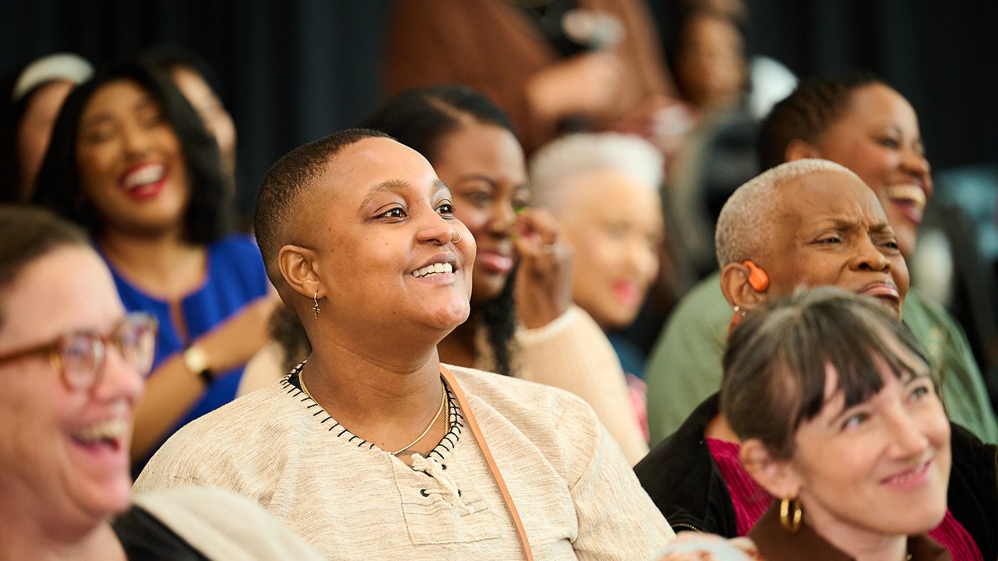 A diverse group of people seated indoors, smiling and laughing. The mood is joyful and lively