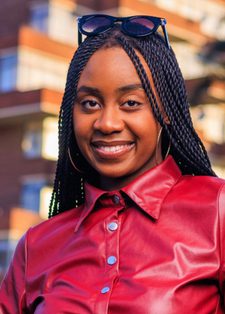Young woman with braided hair and sunglasses on head, wearing a red leather jacket, smiles confidently