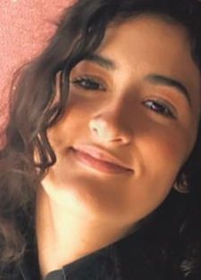 Headshot of a young woman with long, curly dark hair smiling softly