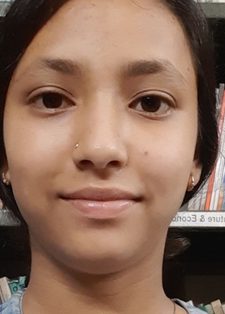 A person with dark hair smiles softly in front of bookshelves