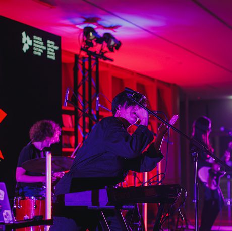 A dynamic live band performs on stage at the Women of the World Festival. Vibrant pink and purple lights illuminate the scene