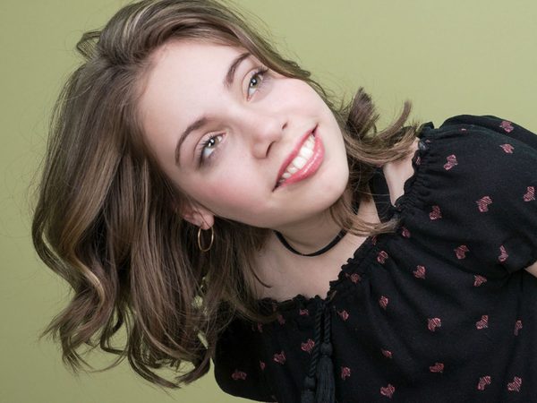 Smiling young woman with wavy brown hair, tilting her head against a green background
