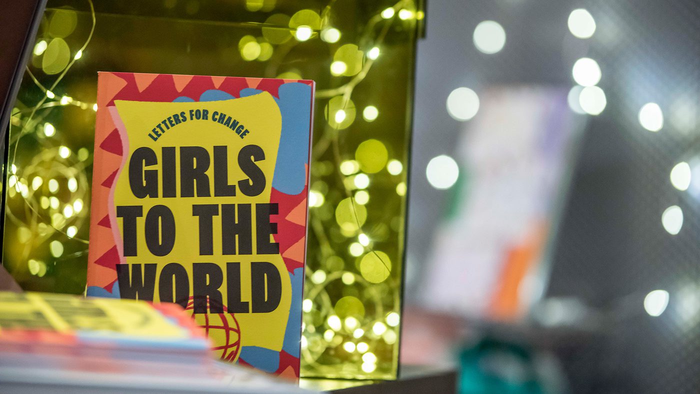 A colourful book titled "Girls to the World" sits amidst soft glowing lights.