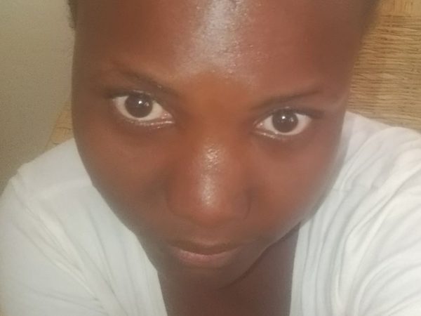 A young woman in a white shirt looks up at the camera with a soft neutral expression