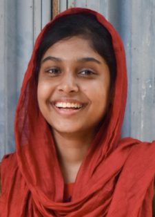 Smiling young woman in a red headscarf stands against a textured grey metal background