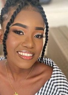 Smiling woman with braided hair and off-shoulder checkered top, sitting in a relaxed setting