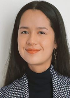 Smiling woman with long dark hair, wearing a black turtleneck and checkered blazer