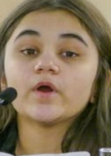 A young person sits between two microphones, speaking with a focused expression