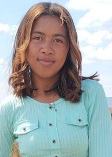 Young woman in a light green shirt stands in a grassy field with scattered trees