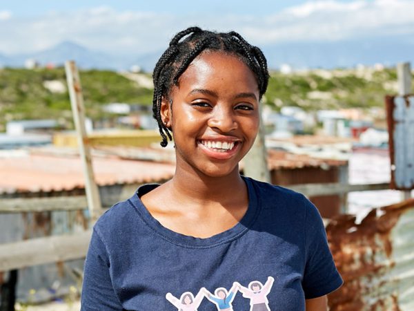 Smiling woman with braided hair stands outdoors in front of a rural landscape