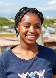 Smiling woman with braided hair stands outdoors in front of a rural landscape