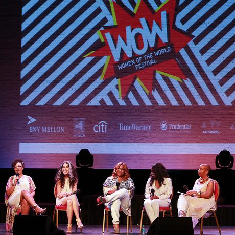 Five women sitting on stage with microphones, smiling and laughing. One of them is currently talking and looking at the audience.