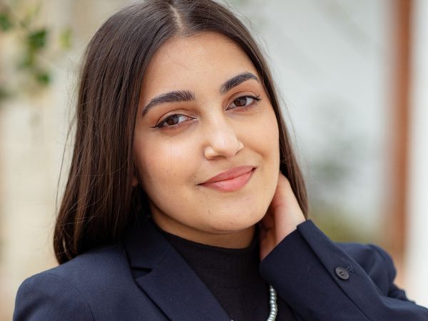 Smiling woman with long brown hair wearing a navy blazer and black top