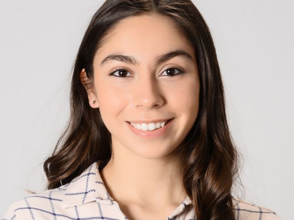 Headshot of Selin Özünaldım smiling in the camera. She has long brown hair and is wearing a cream and blue check top.