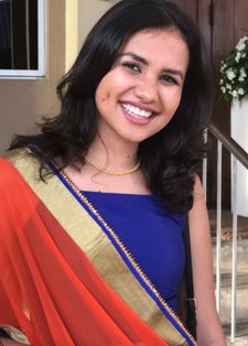 A woman smiles warmly, wearing a vibrant orange and gold sari with a blue blouse