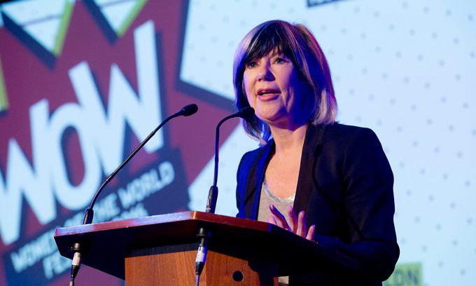A woman wearing a dark suit speaks at a podium with "WOW" displayed on a colourful background.