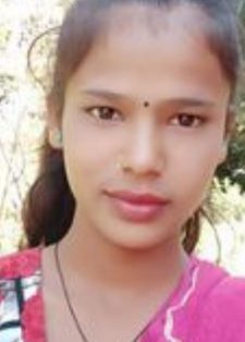 A young woman stands outdoors, wearing a colorful patterned top and a pink scarf