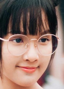 A young person with round glasses and a small smile stands outdoors