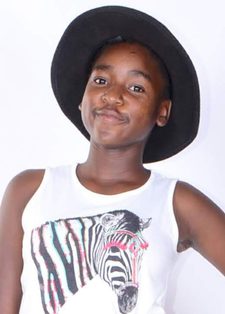 Young girl wearing a black hat and a white tank top with a zebra graphic, poses confidently against a plain backdrop