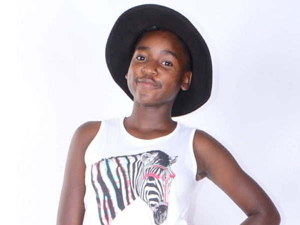 Young girl wearing a black hat and a white tank top with a zebra graphic, poses confidently against a plain backdrop