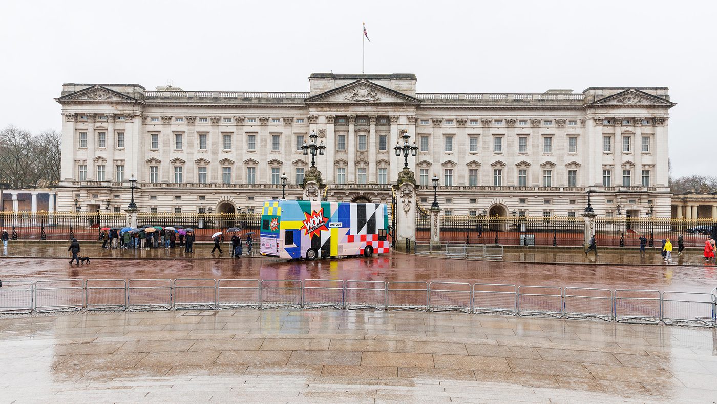 Buckingham Palace on a rainy day, with the colourful WOW bus in front and people holding umbrellas