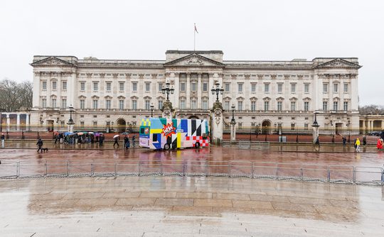 Buckingham Palace on a rainy day, with the colourful WOW bus in front and people holding umbrellas
