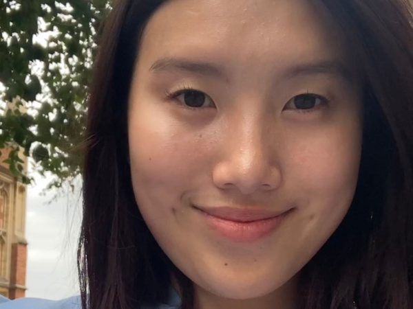 A young woman smiles softly in a close-up portrait outdoors
