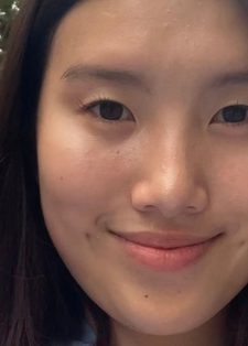 A young woman smiles softly in a close-up portrait outdoors