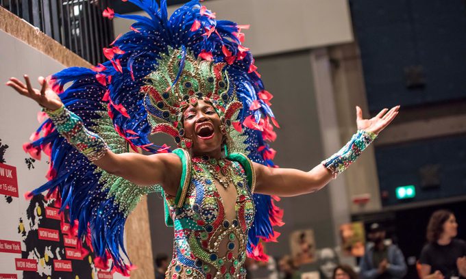 Dancer in vibrant, feathered costume joyfully performs with outstretched arms and smile