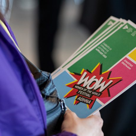 A person in a purple jacket holds colourful brochures for the WOW Women of the World Festival.