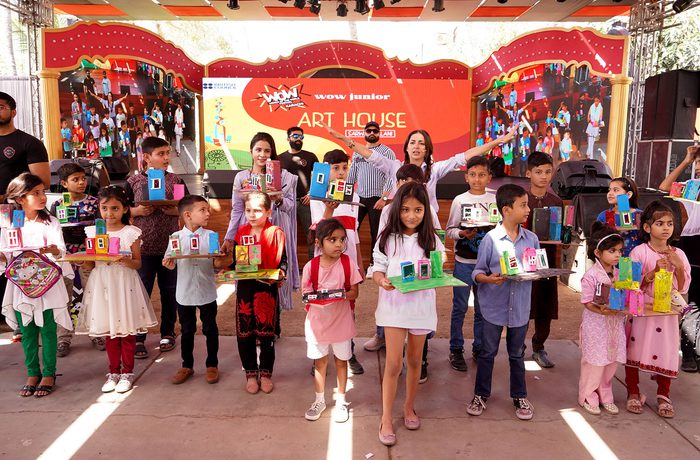 Children proudly display colourful 3D art projects on stage with vibrant decorations