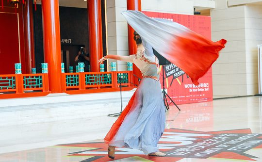 A dancer twirls gracefully in a flowing red and white dress, set against vibrant red columns