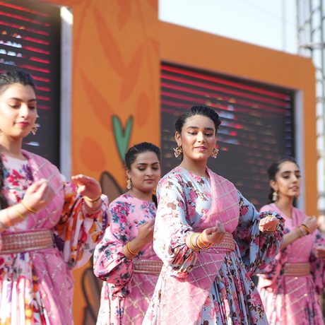 A group of women in pink floral outfits perform a dance onstage. Their expressions are focused and graceful.