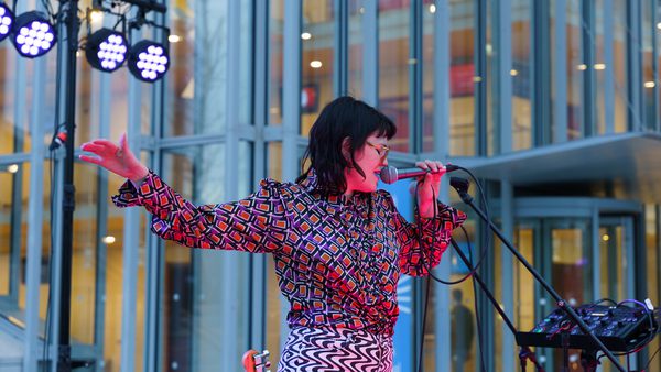 Woman in colourful clothing sings into a microphone, eyes closed, with one arm extended.