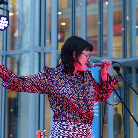 Woman in colourful clothing sings into a microphone, eyes closed, with one arm extended.