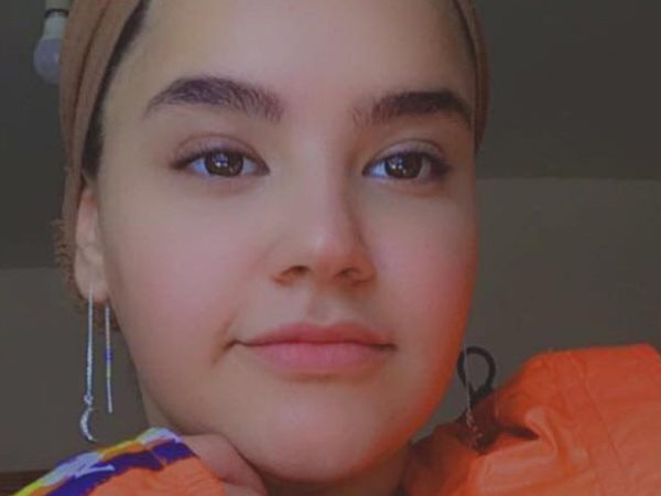 A woman wearing a headscarf and long earrings is shown from the shoulders up.