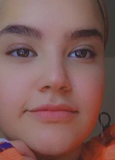 A woman wearing a headscarf and long earrings is shown from the shoulders up.